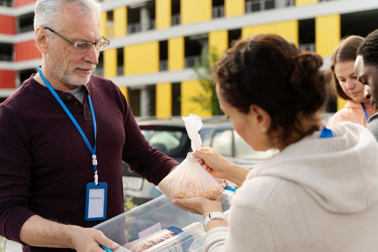 Volunteers sorting food donations at a charity. "Volunteer" ID badge visible.
