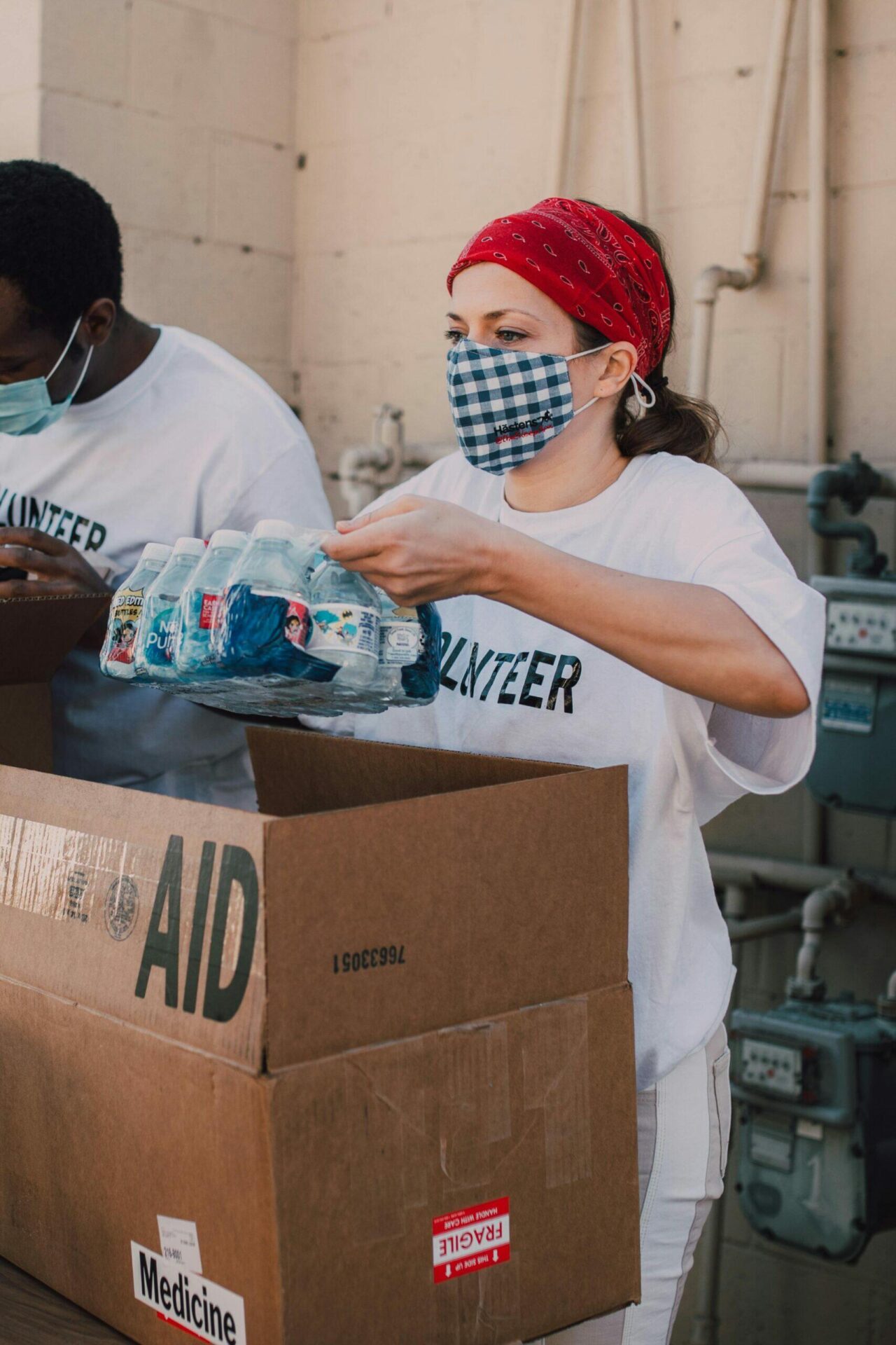 Volunteers wearing masks pack bottled water into an "AID" box marked "Medicine," fulfilling their ACNC and ASIC duties.