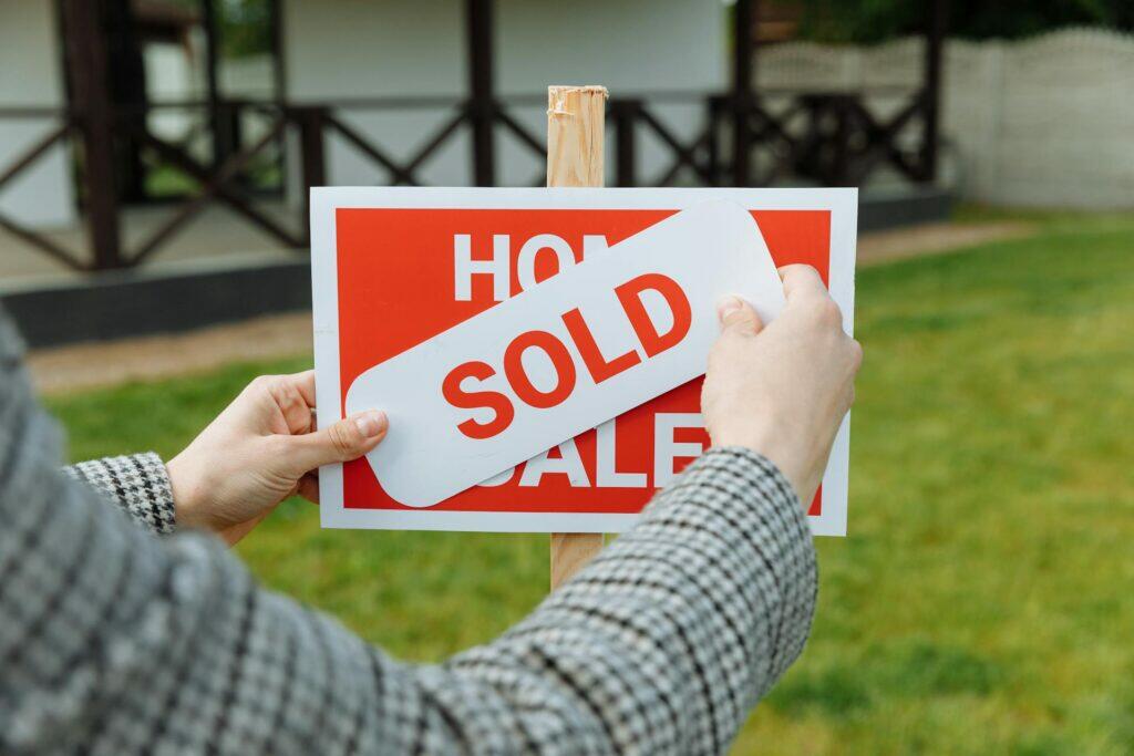 Person placing a "SOLD" sign on a "HOME FOR SALE" real estate sign. Conveyancing lawyers assist with property sales.