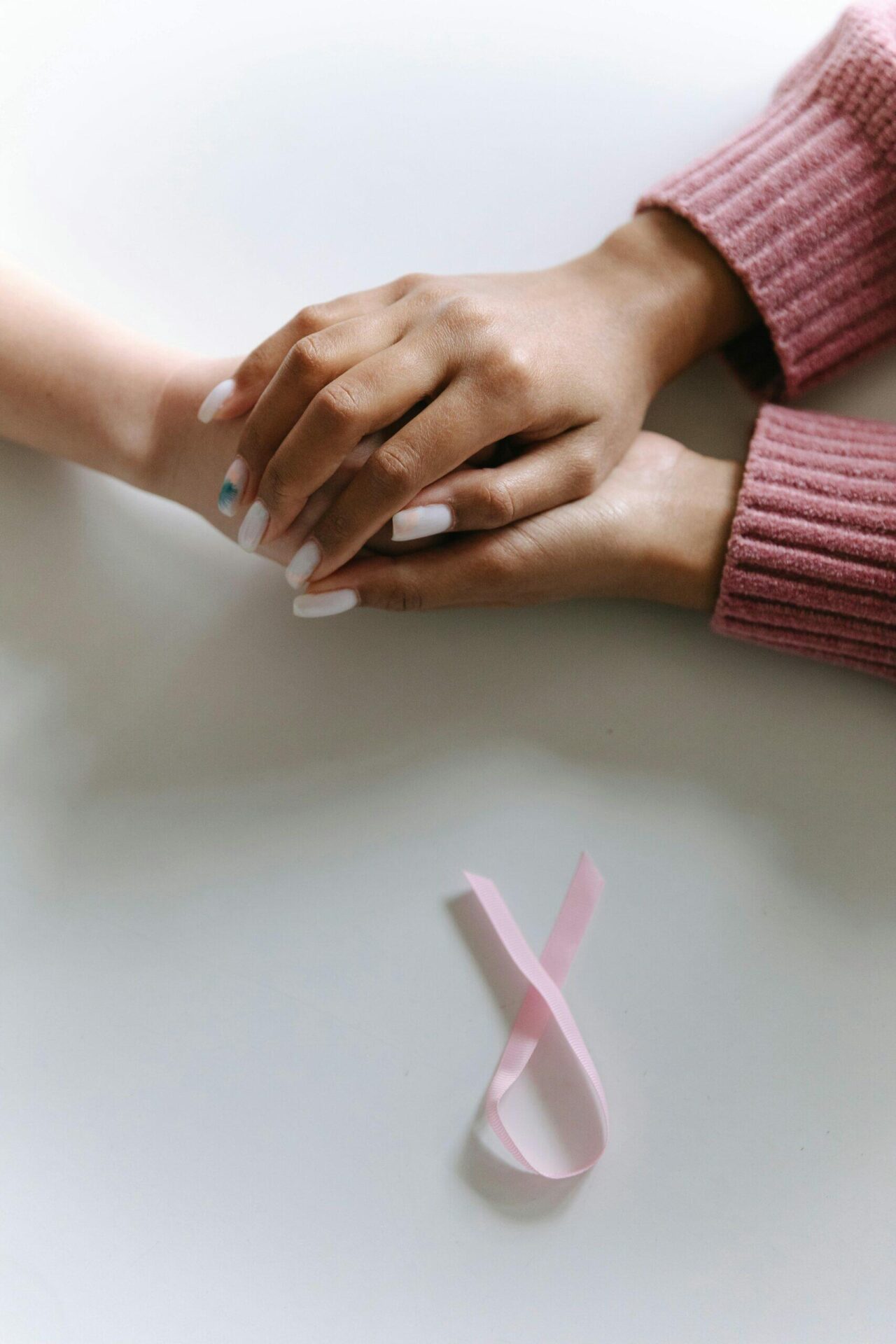 Two hands clasped together, pink ribbon nearby. Supporting cancer charities.