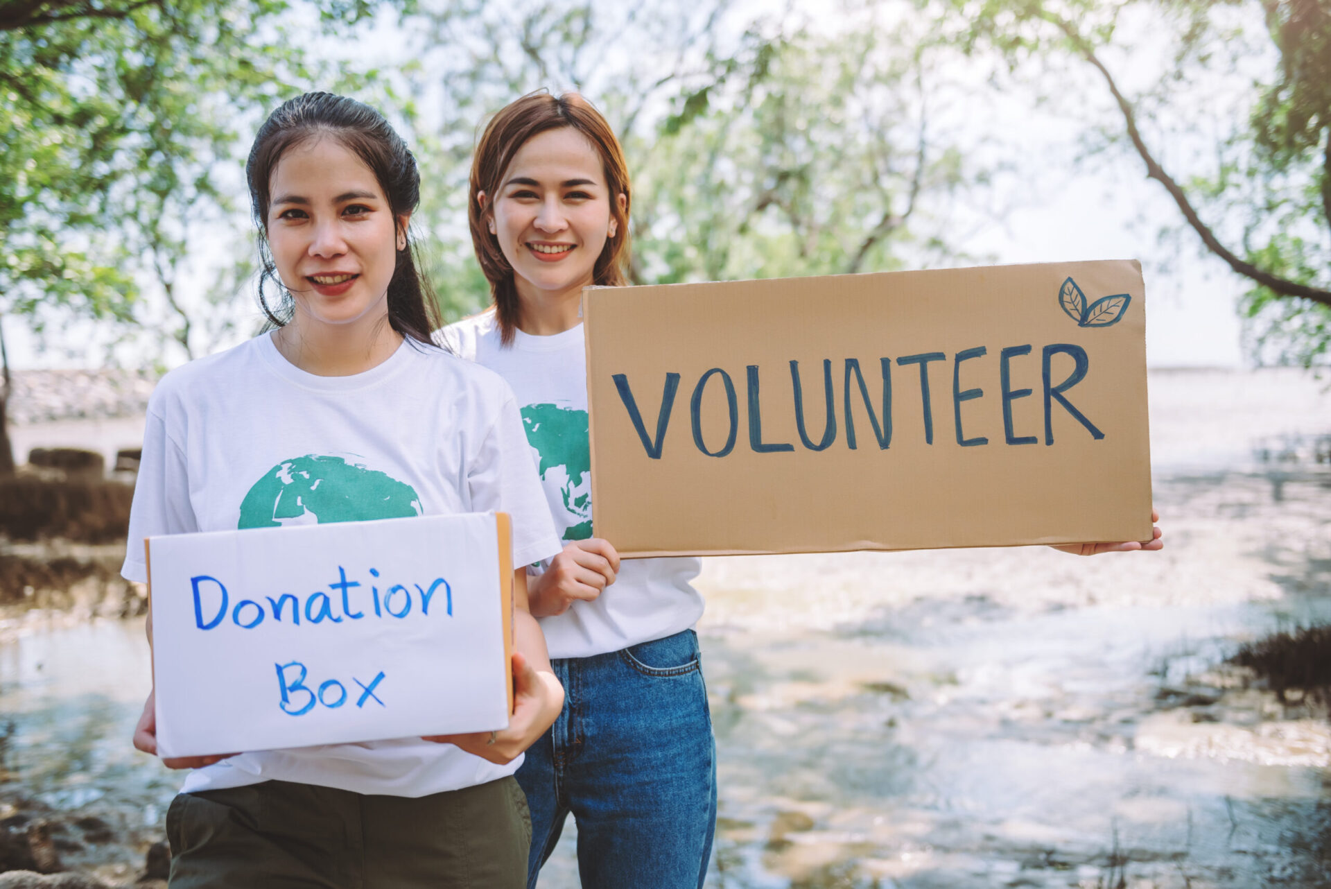 Two women holding signs reading "Donation Box" and "Volunteer" outdoors