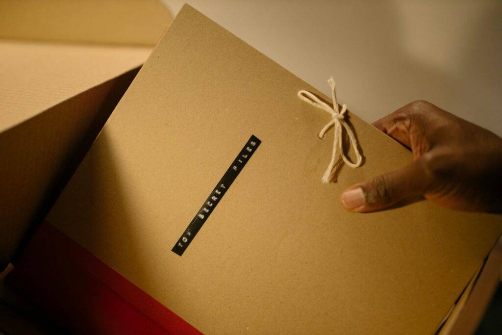 Hand holding a tied manila folder labeled "TOP SECRET FILES".
