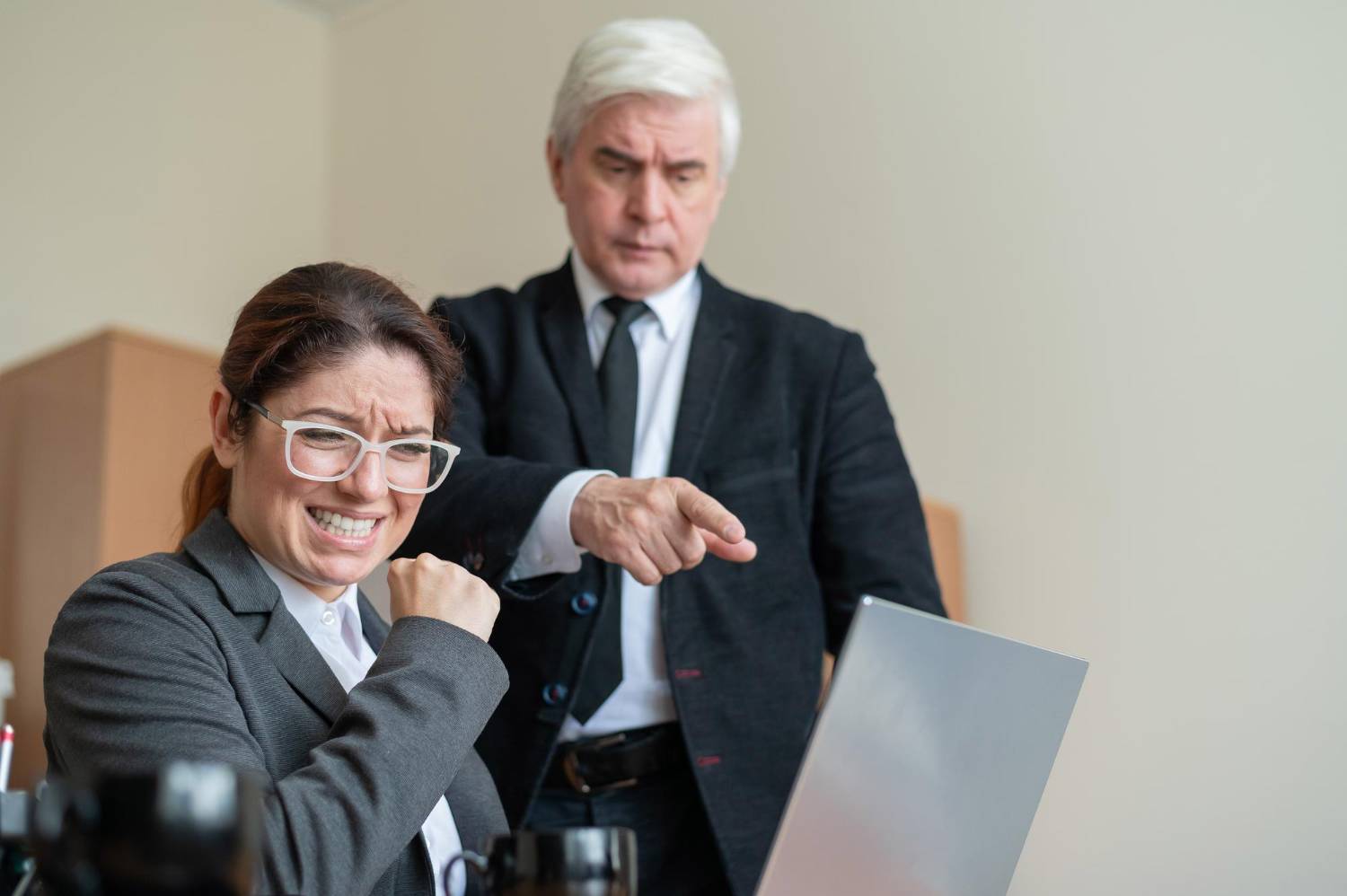 Frustrated woman at laptop being scolded by older boss in suit. Insolvency litigation concept.