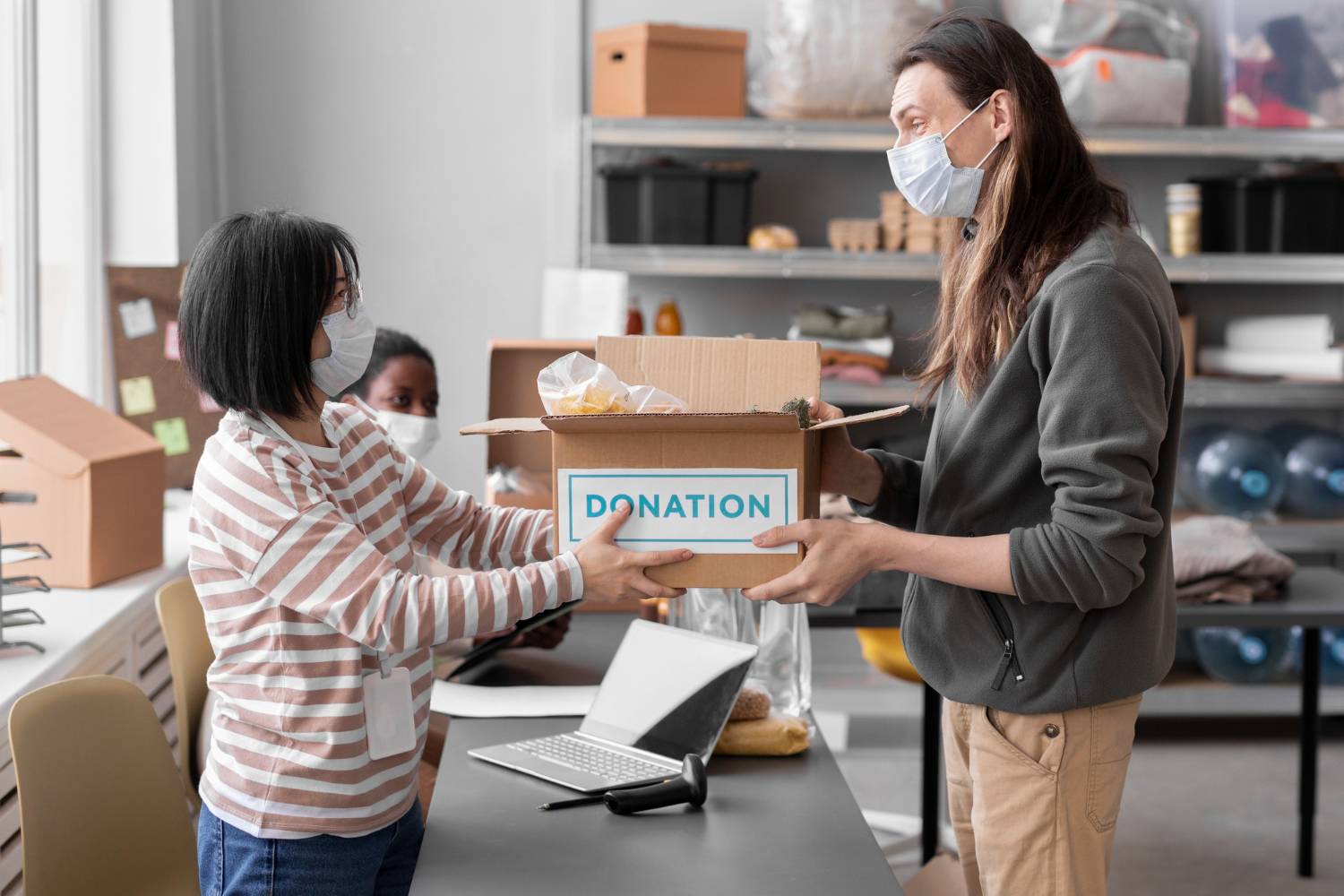 Donation box being handed over by a person wearing a mask. Text on box reads "Donation.