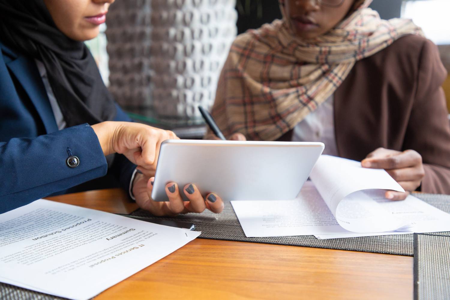 Two Muslim women review Islamic inheritance papers on a tablet. Sharia wills and succession planning.