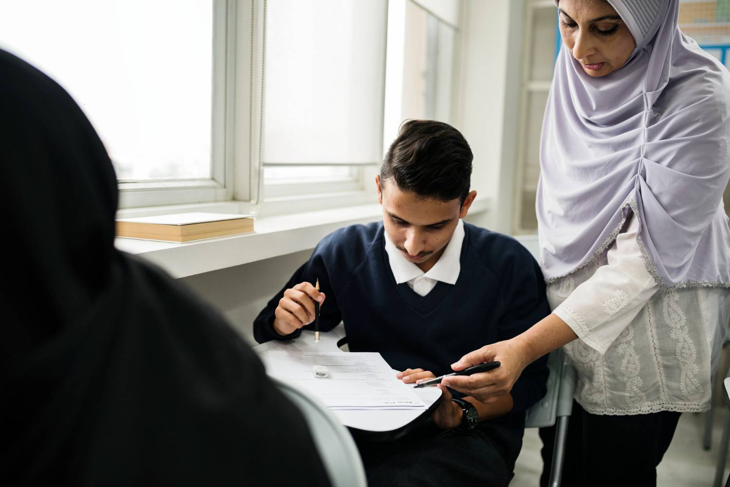 Teacher assisting student with a form, possibly related to Islamic will executor appointment.