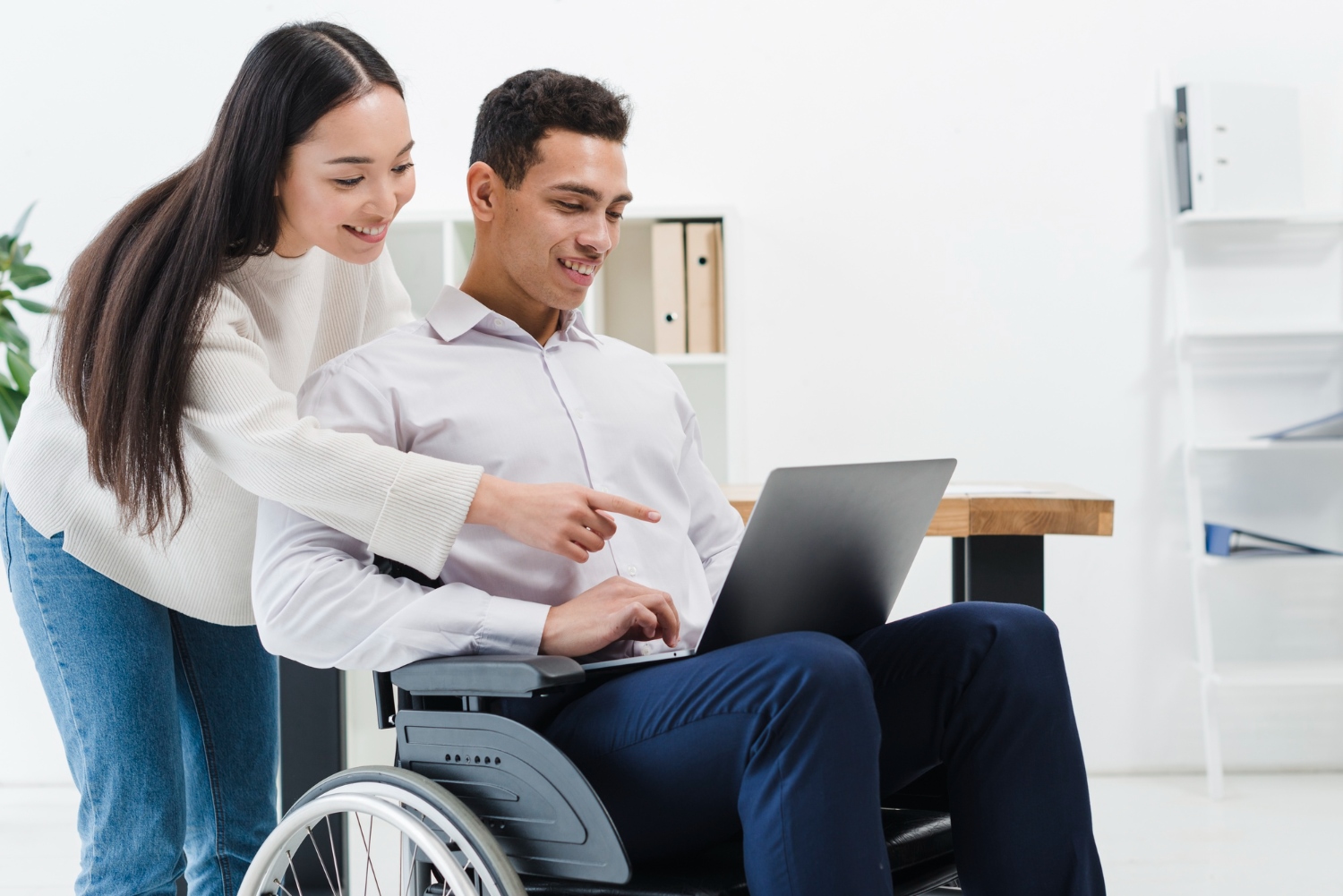 Man in wheelchair works on laptop with colleague. NDIS support.