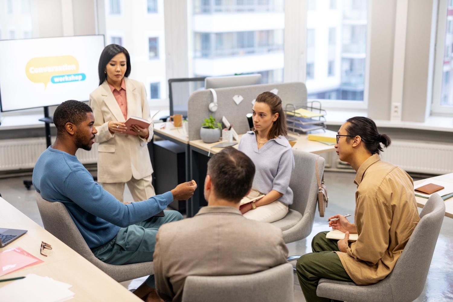 Group at a conversation workshop, led by an Asian woman in a suit. "Conversation Workshop" is on the screen.