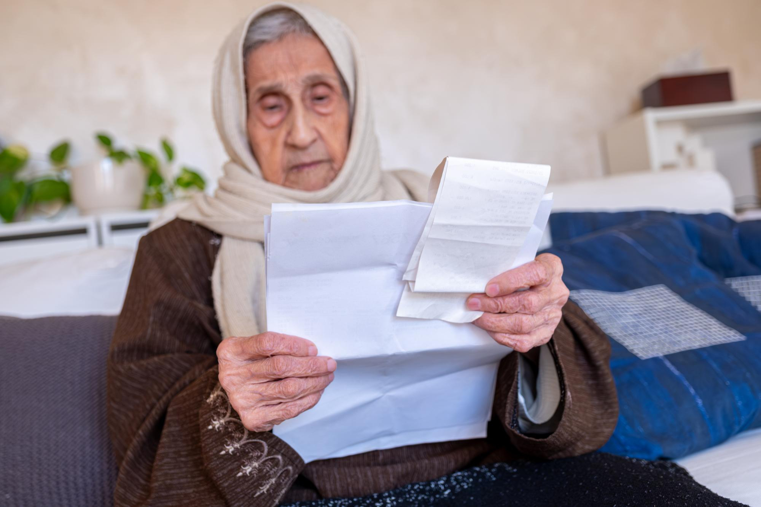 Elderly woman in headscarf reviews documents, possibly related to Islamic will or estate planning.