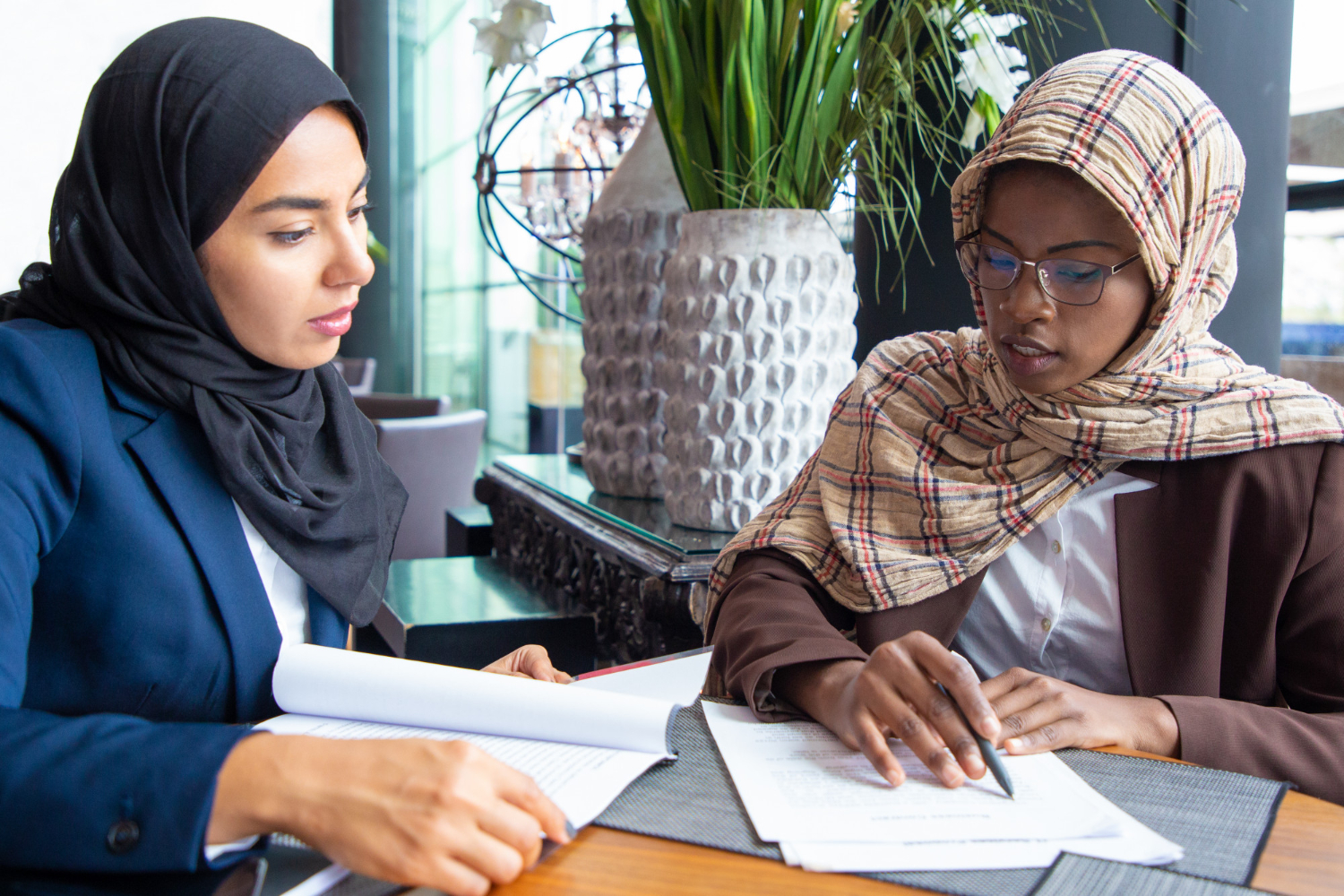 Two Muslim women in hijabs discuss documents, possibly related to Islamic Waqf administration in NSW.