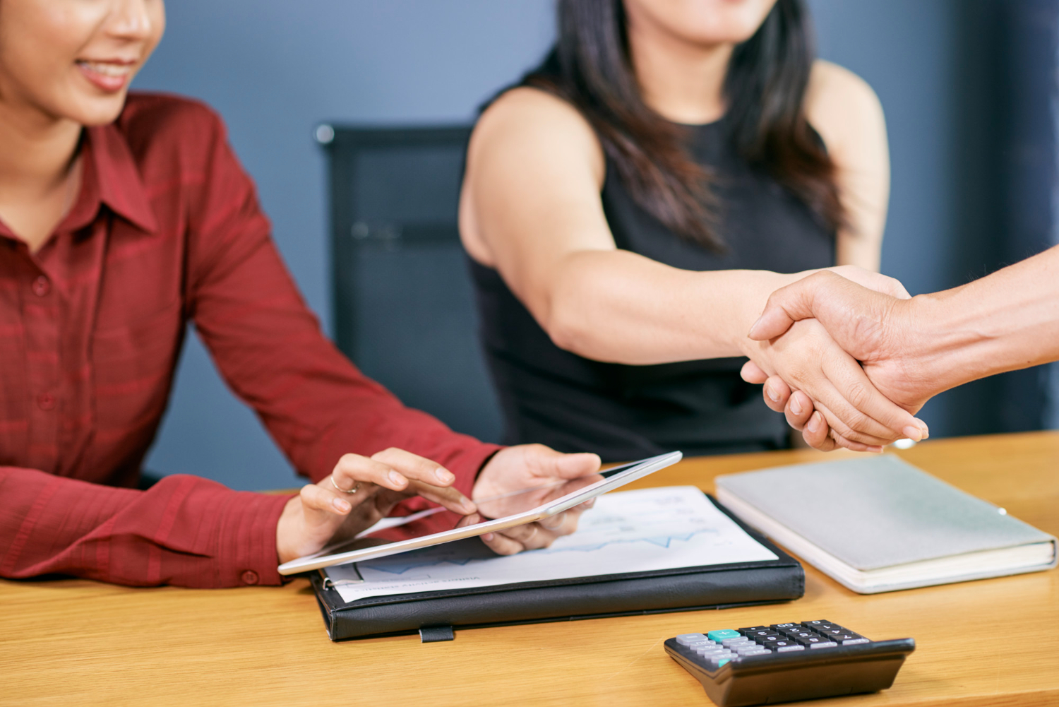 Businesswomen shake hands over tablet discussing consumer guarantee dispute resolution.