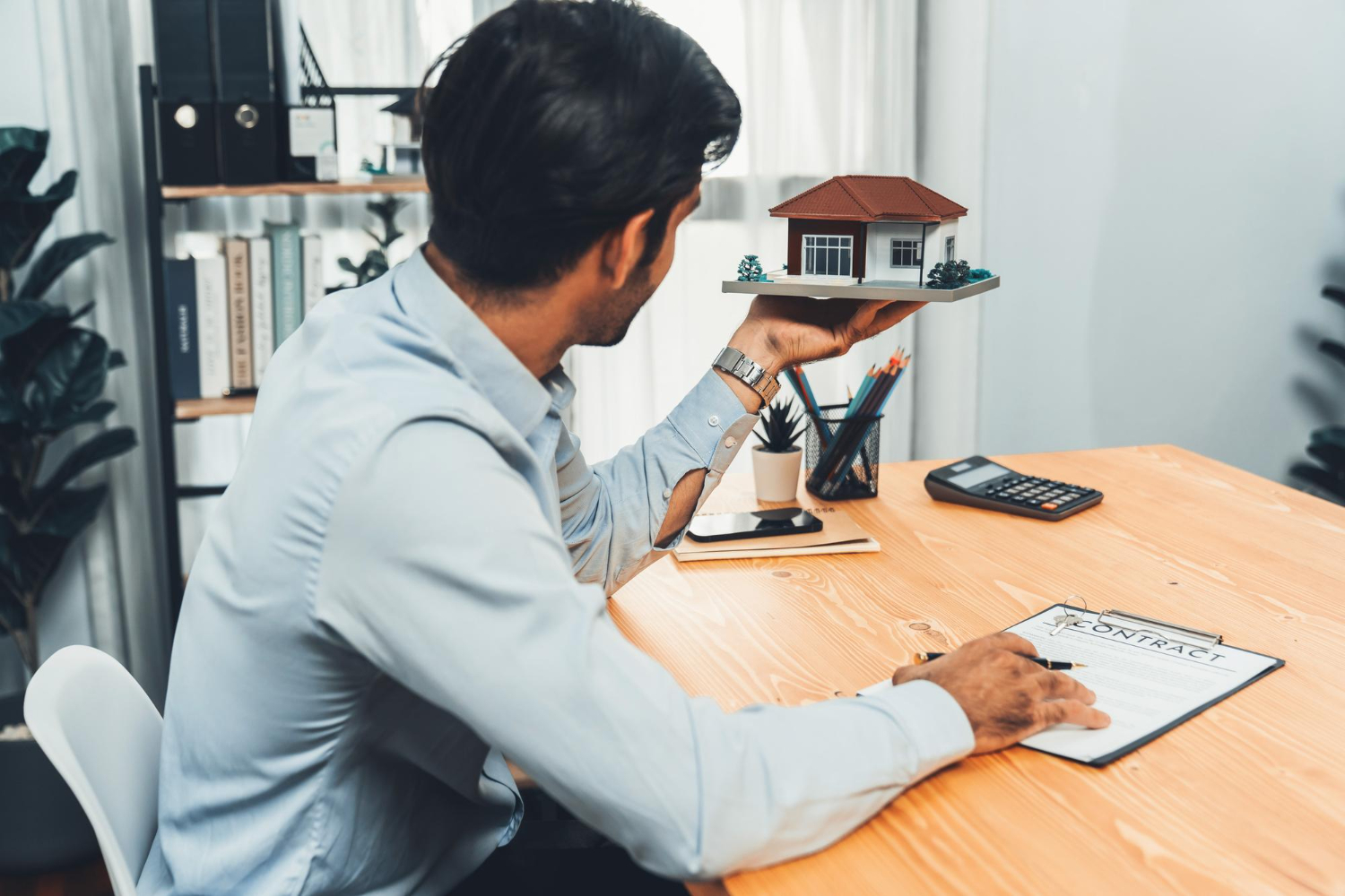 Man with house model and contract, considering estate funding for Iddah maintenance.