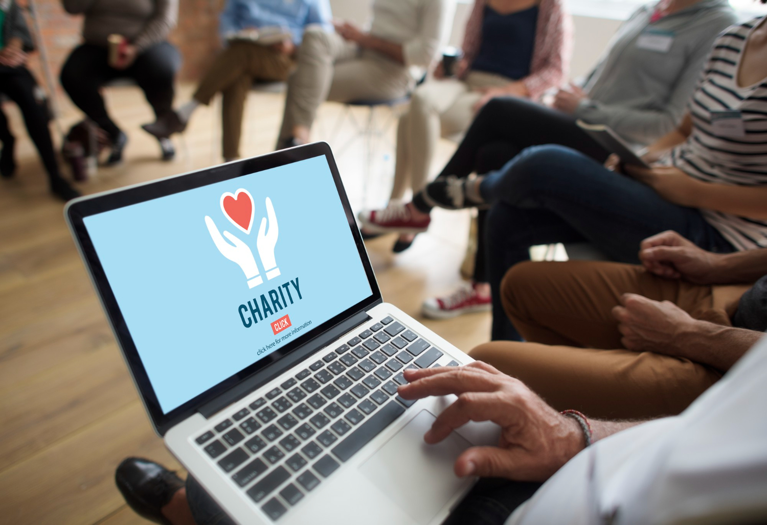 Laptop screen showing 'Charity' with hands holding heart, people in background