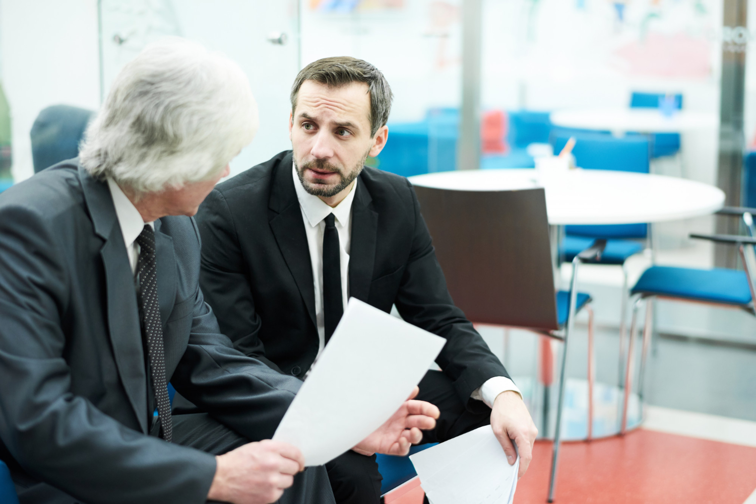 Two businessmen in suits discussing documents in an office