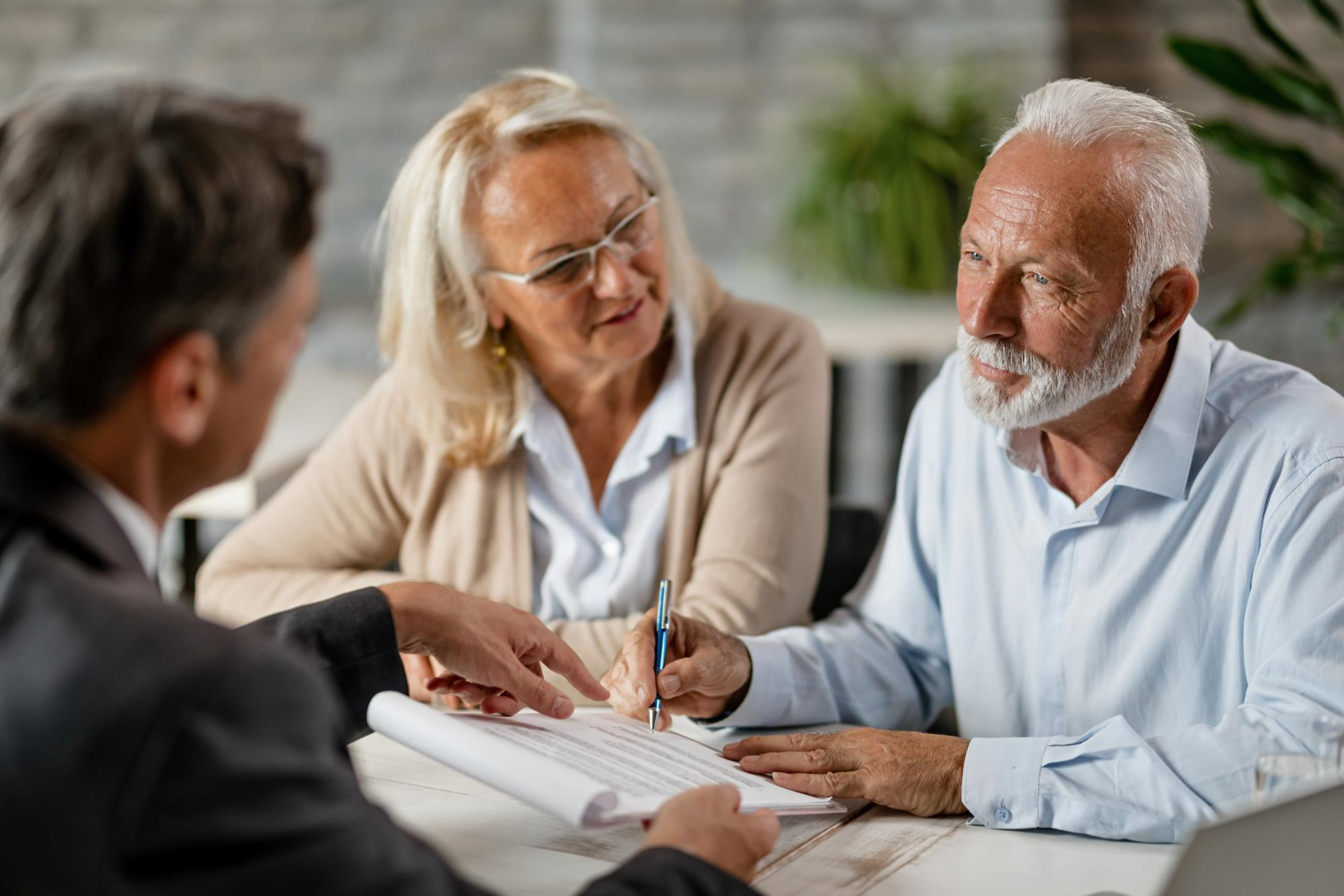 Elderly couple signing documents with financial advisor, discussing superannuation.